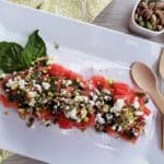 Watermelon salad on a white plate with a bamboo fork and spoon.