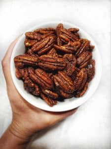 A white bowl filled with candied pecans being held by a hand on a white countertop.