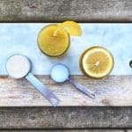 Photo of lemon sugar scrub on a marble slab on a picnic table background. Lemons and measuring spoons with sugar can also be seen.