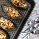 Banana s'mores in a baking pan on a white wood background with four spoons arranged beside it.