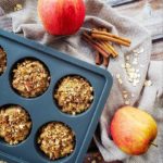 Top-down shot of Apple Pie Protein muffins on a wooden table background with apples and a tablecloth decor.