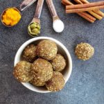 Pumpkin Protein Balls in a bowl on a top-down shot on a grey countertop with measuring spoons filled with spices and cinnamon sticks as decor,