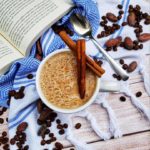 A top-down shot of Mushroom Latte on a fancy cloth with coffee and cacao beans around it. They are on a wooden plank-style table, along with an open book.