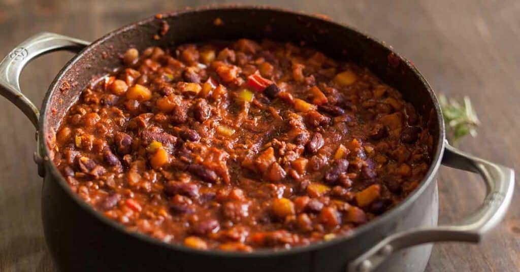 Organic vegetarian chili in iron pot served with rosemary on a distressed wood country table.