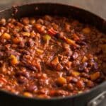 Organic vegetarian chili in iron pot served with rosemary on a distressed wood country table.