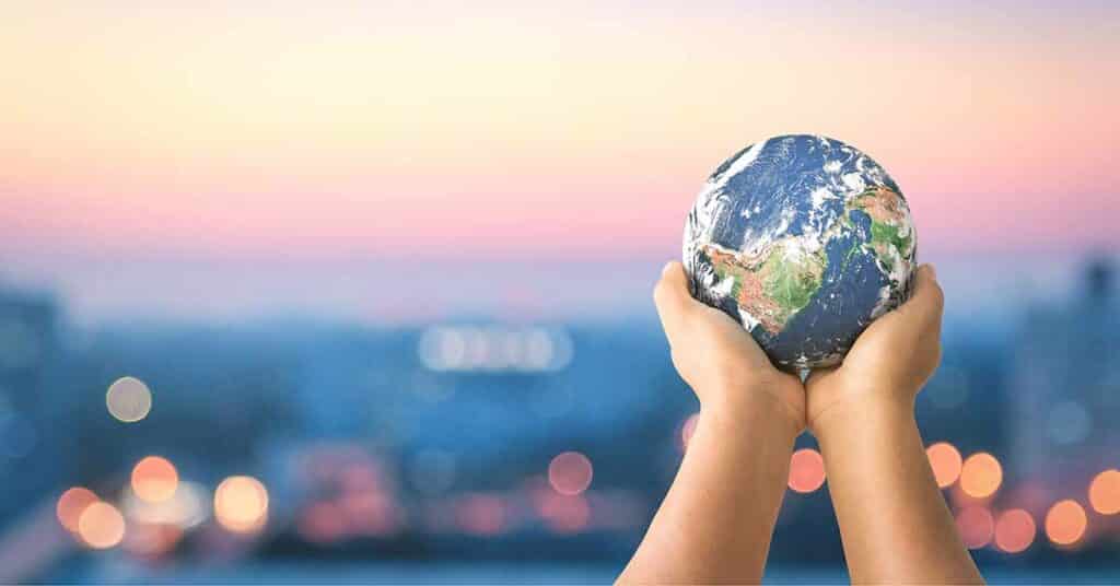 Human hands holding Earth against a blurred cityscape background at dusk.