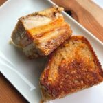 A grilled cheese sandwich on a white plate that's placed on a wooden cutting board.